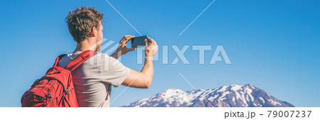 Travel tourist hiking man taking picture with phone of mountains landscape on summer hike adventure. Panorama banner with copy space on blue sky background Travel tourist hiking man taking picture with phone of mountains landscape on summer hike adventure. Panorama banner with copy space on blue sky background 79007237