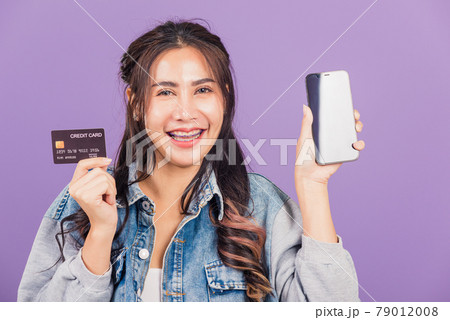 woman confident wear denim jeans shirt smiling show mobile phone blank screen and credit card bank 79012008