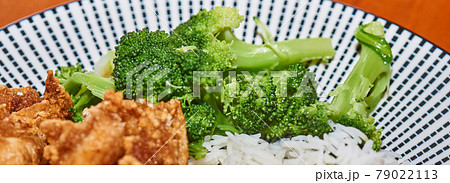 Close-up of cooked green broccoli at the edge of a plate with rice and fried meat Close-up of cooked green broccoli at the edge of a plate with rice and fried meat 79022113