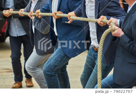 Men with business clothing and formal jackets pulling together on a thick rope, concept photo of the expression "pulling together". 79022707