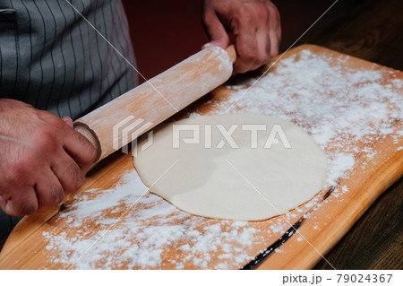 hands roll the dough into a thin layer. Cooking pizza, noodles or pitta at home hands roll the dough into a thin layer. Cooking pizza, noodles or pitta at home 79024367