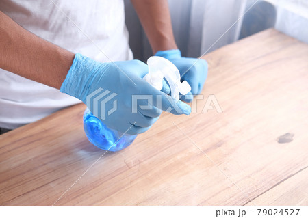 hand in blue rubber gloves holding spray bottle cleaning table  79024527