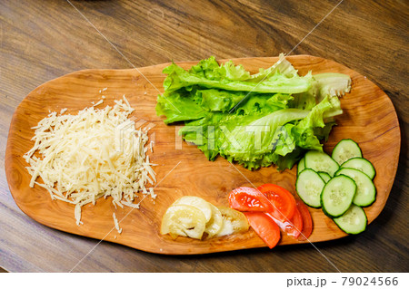 grated cheese, lettuce, ringed tomato and cucumber on a wooden cutting board. grated cheese, lettuce, ringed tomato and cucumber on a wooden cutting board. 79024566