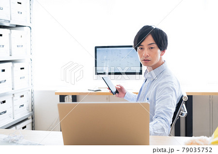2台のパソコンとスマホを操作するエンジニアの男性 79035752