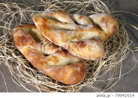 two white bread lying in straw on grey linen tablecloth 79042014