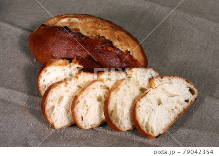 sliced white bread lying in straw on grey linen tablecloth sliced white bread lying in straw on grey linen tablecloth 79042354
