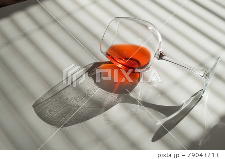 A glass of red wine lies on its side on a white table with a shade from the blinds 79043213