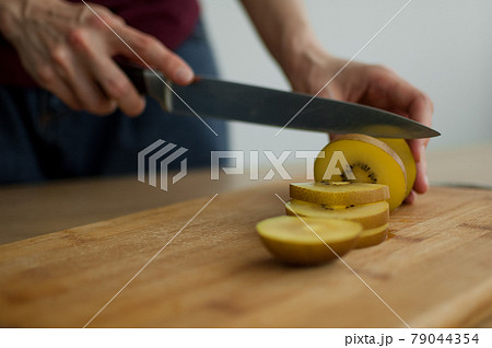 Female hands is cutting a fresh ripe golden kiwi fruit on a cut wooden board. Exotic fruits, healthy eating concept Female hands is cutting a fresh ripe golden kiwi fruit on a cut wooden board. Exotic fruits, healthy eating concept 79044354