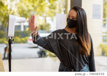 Woman wearing face mask and measuring body temperature while entering restaurant for protection 79046550