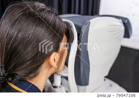 health care, medicine, people, eyesight and technology concept - Young woman checks his vision on the machine checking patient vision at eye clinic or optics store. face close-up 79047106