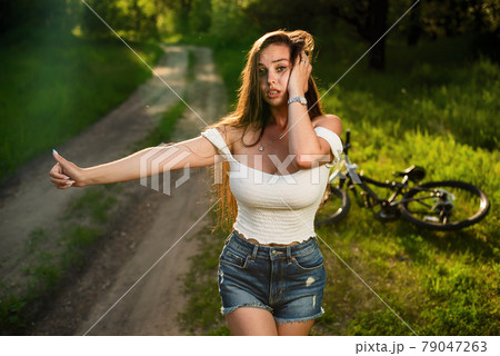 Young sexy woman with broken bike and looking for help raising her thumb up Young sexy woman with broken bike and looking for help raising her thumb up 79047263