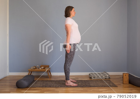 Pregnant woman doing yoga, pilates training, standing in tadasana, mountain pose 79052019