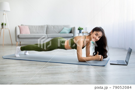 Full length of young Indian woman standing in elbow plank on sports mat, doing abs exercise indoors Full length of young Indian woman standing in elbow plank on sports mat, doing abs exercise indoors 79052084