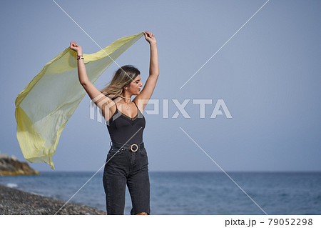 young woman dancing on the beach with a yellow scarf 79052298