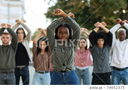 Black lady guiding multiracial group of activists, rasising fists up 79052375