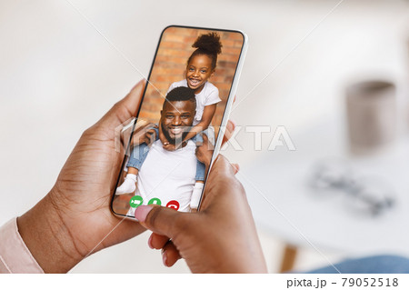 Black woman video conferencing with her cheerful husband and daughter, using smartphone to speak to her family from home Black woman video conferencing with her cheerful husband and daughter, using smartphone to speak to her family from home 79052518