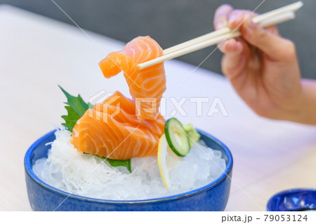 Hand holding salmon sashimi using chopsticks - Raw fresh salmon sliced served on ice with wasabi, Japanese food style. 79053124