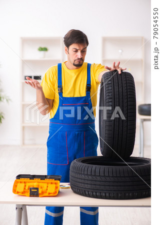 Young male garage worker with tyre at workshop Young male garage worker with tyre at workshop 79054550