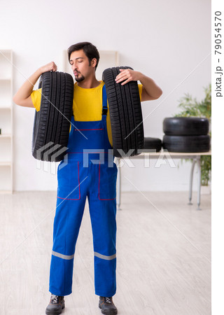 Young male garage worker with tyre at workshop 79054570
