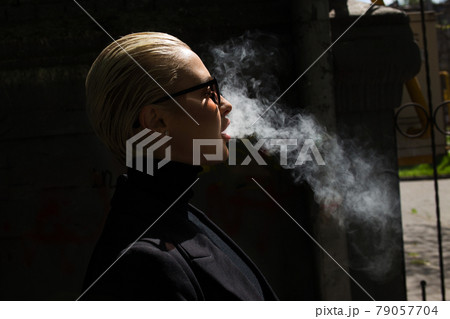A beautiful girl smokes a vape and lets out smoke 79057704