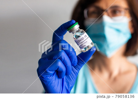 Middle age female nurse in safety mask and gloves holds bottle with liquid COVID vaccine for injections 79058136