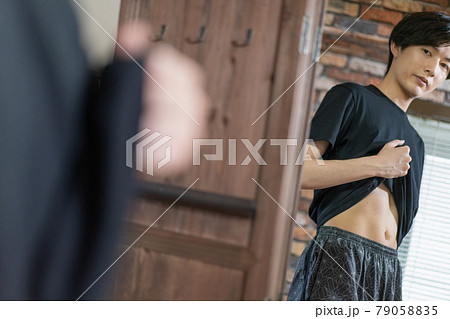 鏡でお腹の贅肉をチェックする若い男性 79058835