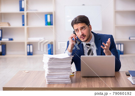 Young male employee unhappy with excessive work in the office Young male employee unhappy with excessive work in the office 79060192