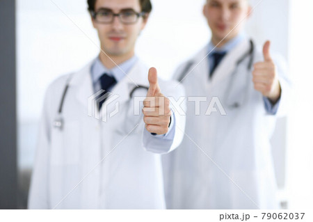 Two male doctors standing as a team and showing thumbs up as a symbol of the best service for patients in the clinic. Medicine and health care 79062037