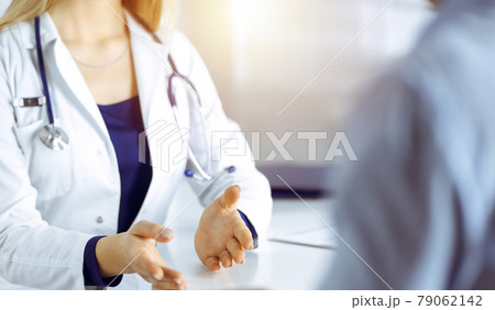 Unknown woman-doctor is talking to her patient, while they are sitting together in the sunny cabinet in a clinic. Female physician with a stethoscope at work, close-up. Perfect medical service in a 79062142