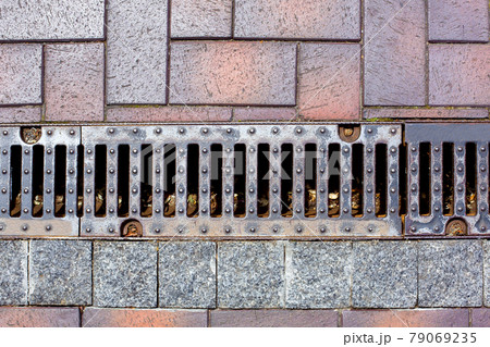 an iron drainage grate of a rain channel on a pedestrian sidewalk made of stone tiles urban landscaping infrastructure of parks. 79069235