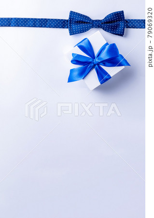 Father day gift. White box with bow ribbon, blue bowtie or tie on light background. Concept of Fathers Day greeting card, copy space for text. Father day gift. White box with bow ribbon, blue bowtie or tie on light background. Concept of Fathers Day greeting card, copy space for text. 79069320