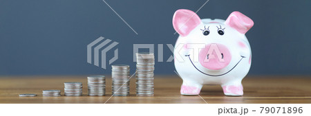 Pink piggy bank standing on table near heaps of coins 79071896