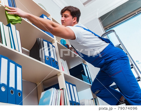 Male office cleaner cleaning shelves in office Male office cleaner cleaning shelves in office 79074096