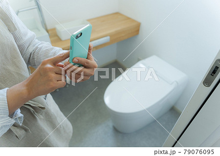 トイレとスマホを持つ手元カット 79076095