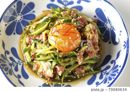 卵黄や糸唐辛子やいり胡麻が乗っている胡瓜と生ハムのユッケを白背景で俯瞰撮影 79080639