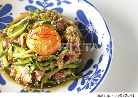 卵黄や糸唐辛子やいり胡麻が乗っている胡瓜と生ハムのユッケを白背景で俯瞰撮影 79080641