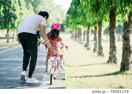 Father Teaching daughter To Ride Bike In the park Father Teaching daughter To Ride Bike In the park 79085249