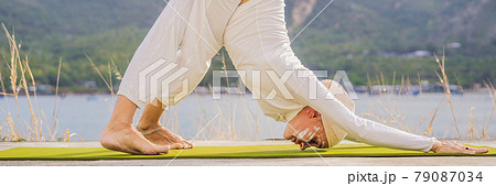 BANNER, LONG FORMAT Kundalini yoga woman in white clothes and turban practices yoga kundalini on the background of the sea, mountains and sunset. Fighting face painting of the Indians shows her inner 79087034