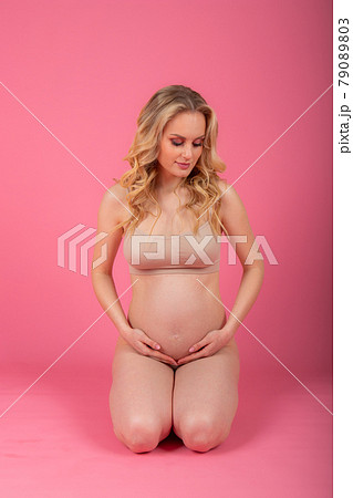beautiful young pregnant woman sitting on the floor, on a pink studio background beautiful young pregnant woman sitting on the floor, on a pink studio background 79089803