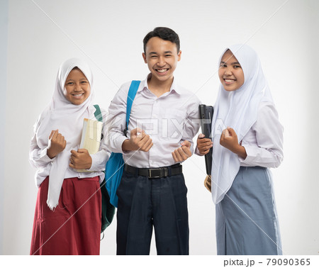 Three teenagers in school uniforms smiled with excited hands gesture when carrying a backpack and a book 79090365