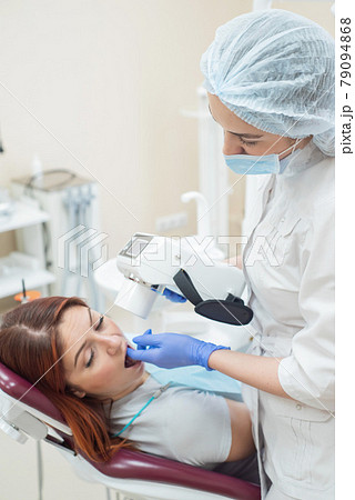 Attractive smiling woman doctor in a white uniform with tools in hand. Young beautiful female dentist takes jaw x-ray of female patient. Attractive woman patient at dentist taking x-ray exam. Attractive smiling woman doctor in a white uniform with tools in hand. Young beautiful female dentist takes jaw x-ray of female patient. Attractive woman patient at dentist taking x-ray exam. 79094868