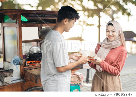 muslim woman ordering chicken satay from small food cart seller. 79095347