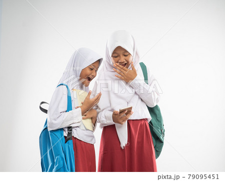 two veiled girls wearing elementary school uniforms using a mobile phone together with shocked expression two veiled girls wearing elementary school uniforms using a mobile phone together with shocked expression 79095451