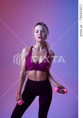 Young woman with dumbbells, neon background 79095857