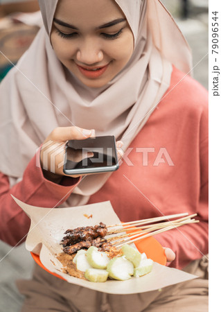 chicken satay buyer taking photo of her food using smart phone 79096544