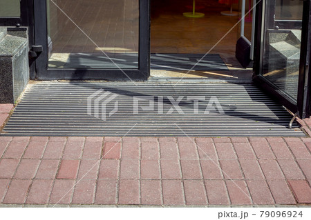 entrance to the store from a pedestrian sidewalk from a plink on a foot mat through a glass door, the facade of the exterior of a building close-up in sunny weather nobody. entrance to the store from a pedestrian sidewalk from a plink on a foot mat through a glass door, the facade of the exterior of a building close-up in sunny weather nobody. 79096924