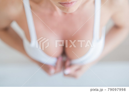 Breast of a sexy young woman, top view. The girl erotically removes the white top in a white studio. Close-up. Blurred focus. 79097998