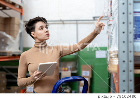 Young female logistics manager standing by rack 79102480