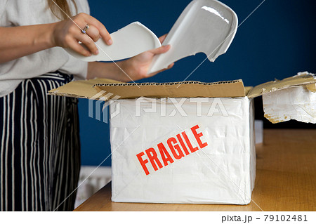 Young woman opening damaged delivery package,online shopping package. Broken fragile plate at home 79102481