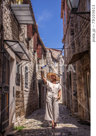 Beautiful blonde young female traveler wearing straw sun hat, taking selfie while sightseeing and enjoying summer vacation in an old traditional costal town at Adriatic cost, Croatia. 79103613